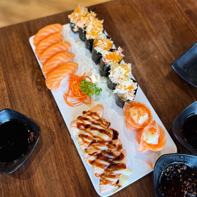 Assorted sushi platter on a white rectangular plate with soy sauce bowls on a wooden table