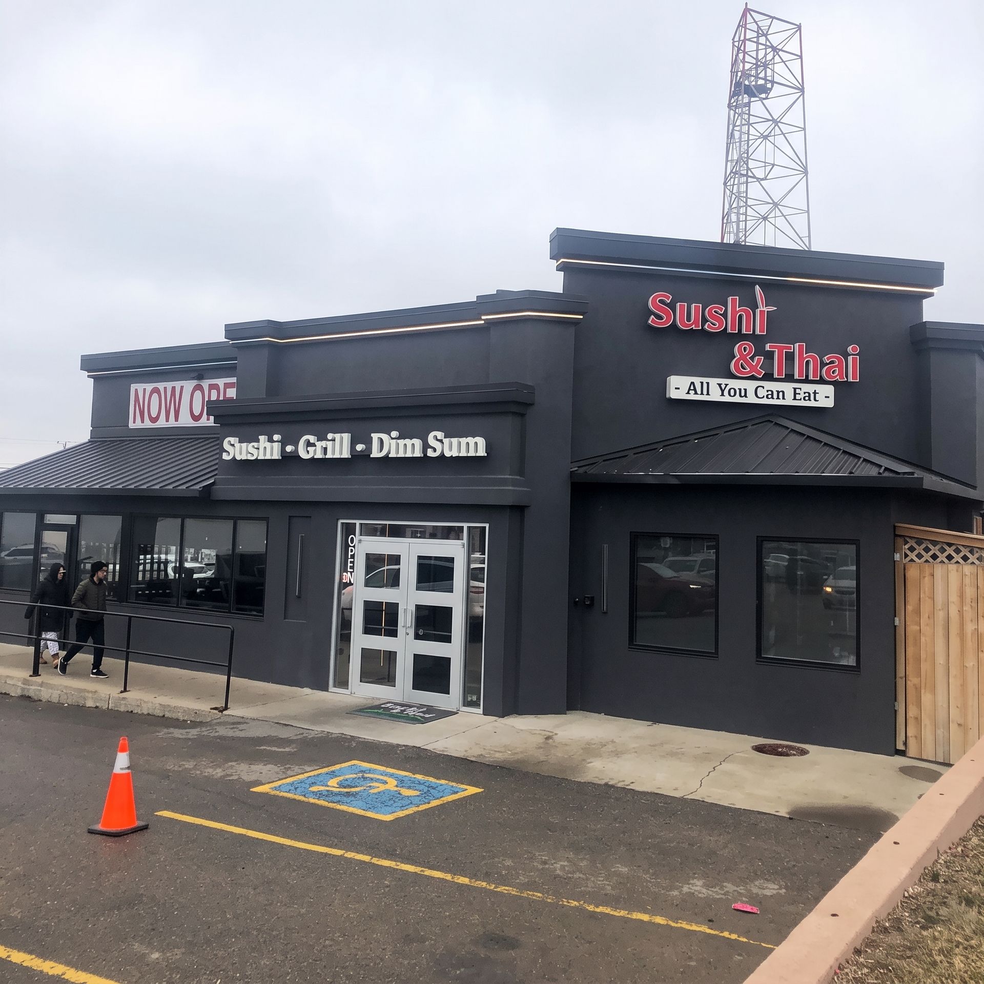 Exterior of Sushi Thai restaurant in a dark gray building with signs and accessible parking spaces.