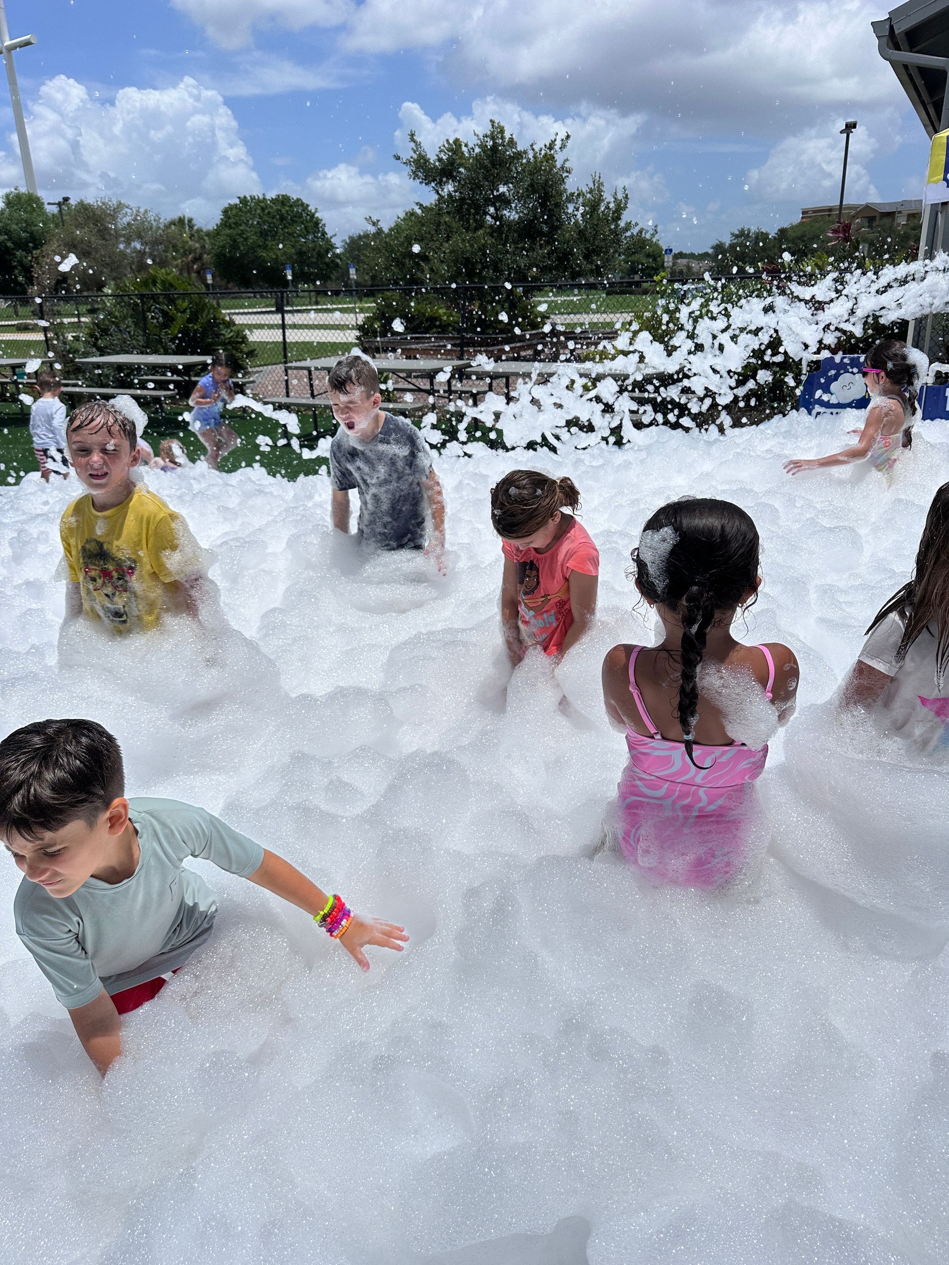 Children play in a large foam party outdoors on a sunny day.