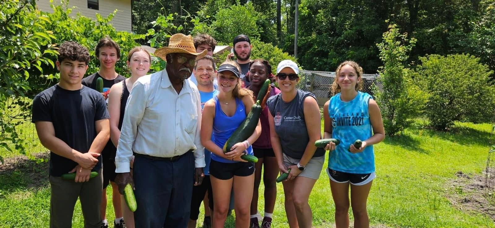 A group of people holding freshly harvested zucchini in an outdoor garden setting.