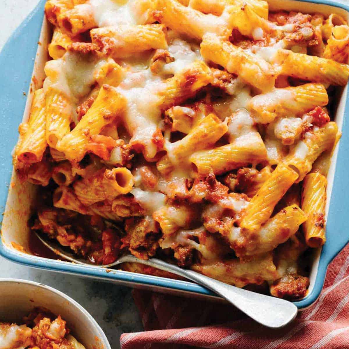 Baked rigatoni pasta with tomato sauce, ground meat, and melted cheese in a blue-rimmed rectangular casserole dish.