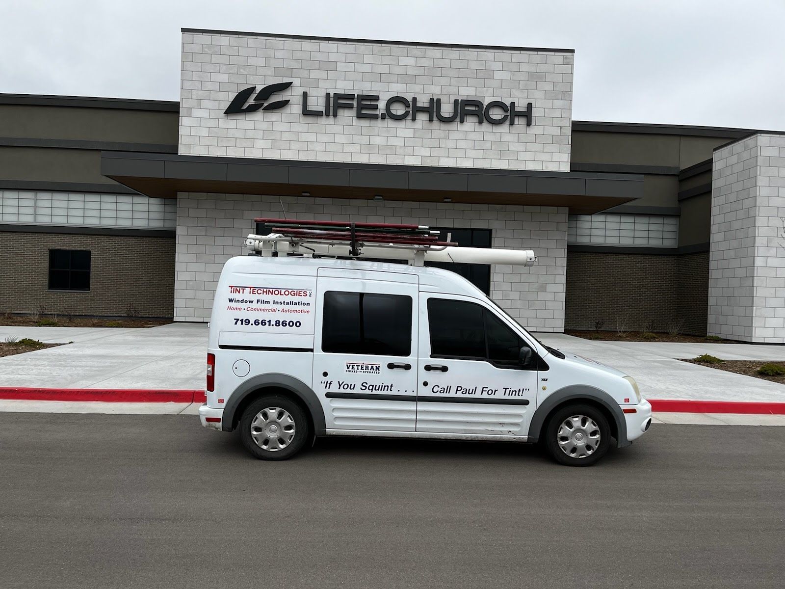 A white van from Tint Technologies in Colorado Springs is parked in front of a life church building.