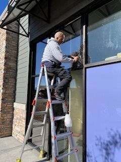A man is standing on a ladder cleaning a window after installing window tint