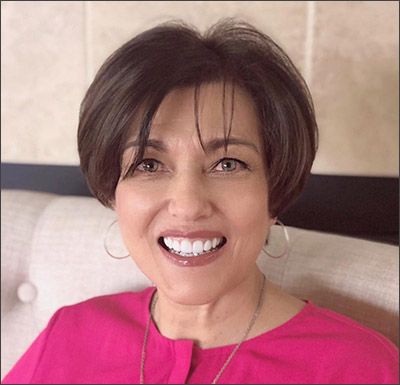 A woman in a pink shirt is smiling for the camera while sitting on a couch.