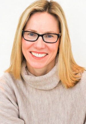 A woman wearing glasses and a sweater is smiling for the camera.