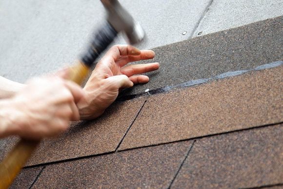 Roofing work on brown shingles, with hands using a hammer and pry bar near a roof seam