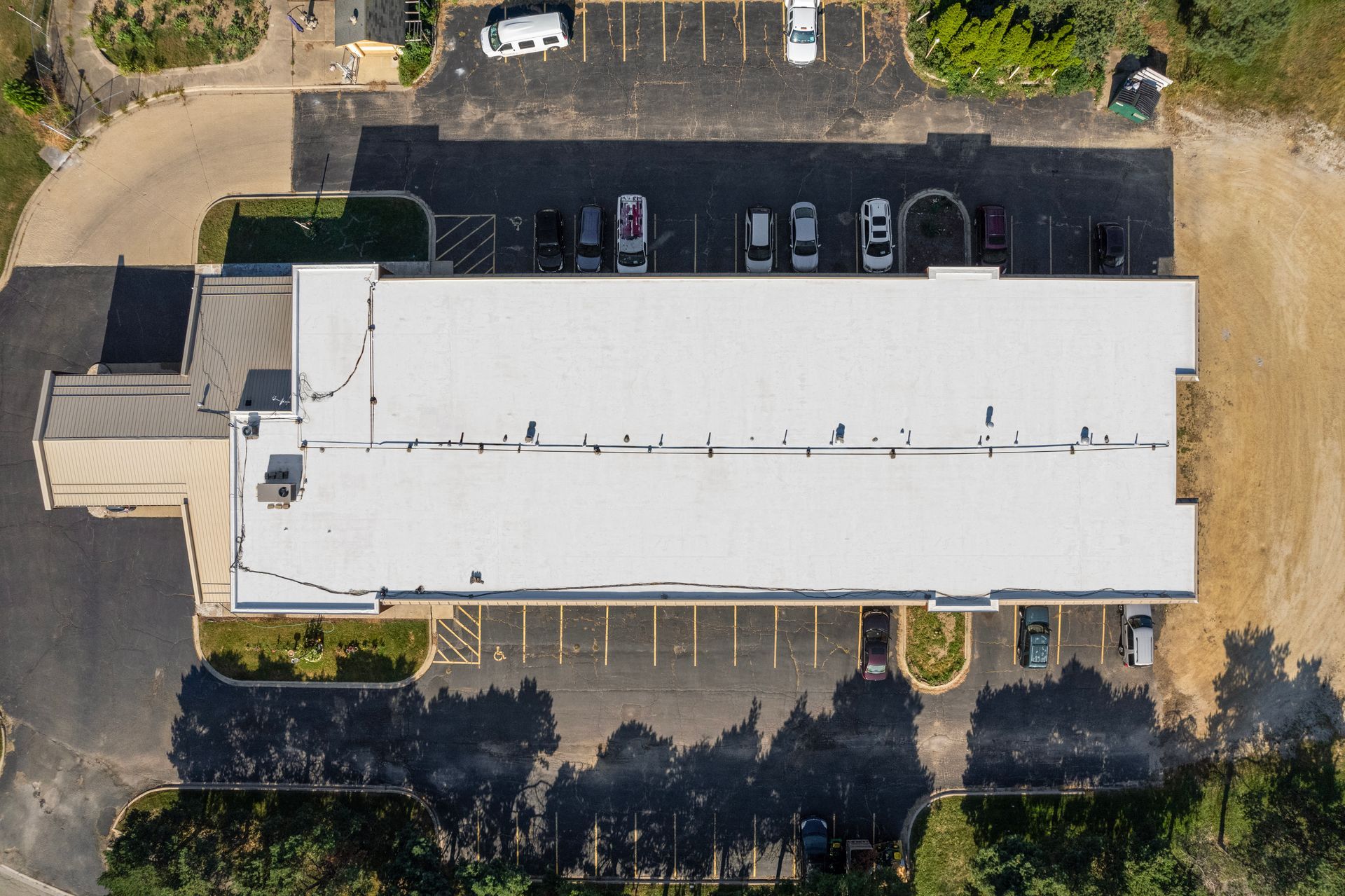 Aerial view of a white-roofed building with parked cars and trees around it.