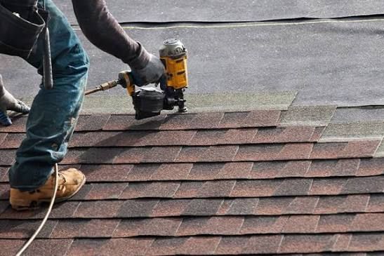 Worker nailing shingles on a roof with a yellow power nailer