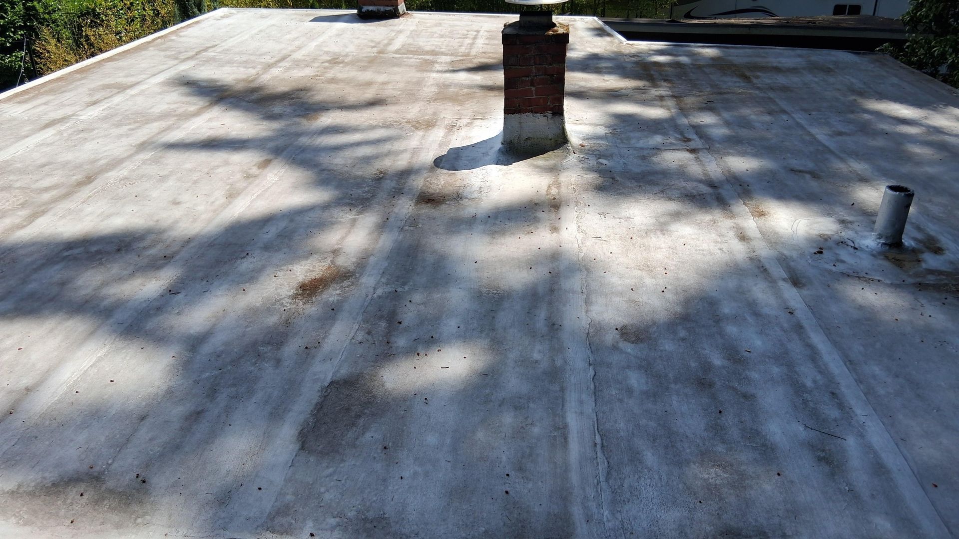Flat rooftop with a brick chimney and vent pipes casting long shadows in bright sunlight.