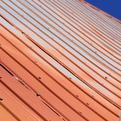 Close-up of an orange corrugated metal roof with blue sky in the corner