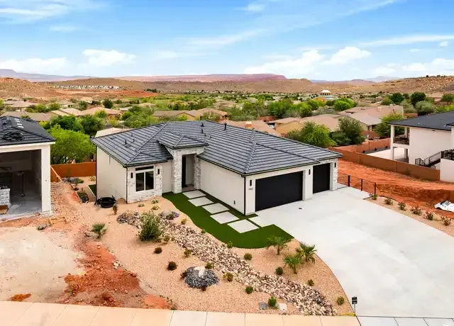A modern gray-roofed house with a two-car garage in a desert neighborhood under a clear sky.