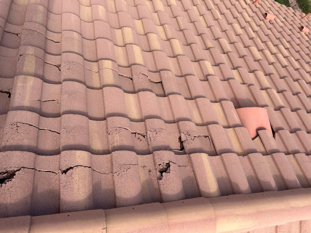 Damaged terracotta roof tiles with cracks and missing pieces on a house roof