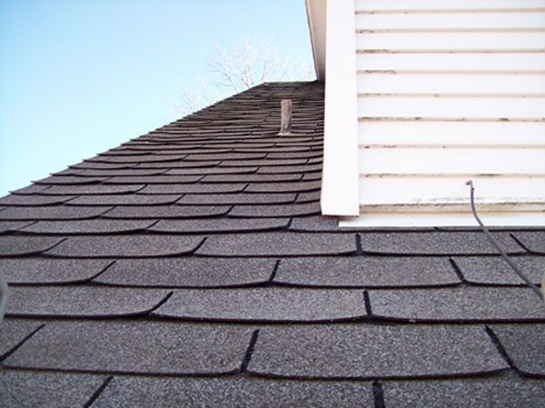 Roof shingles meeting a white-sided dormer under a blue sky