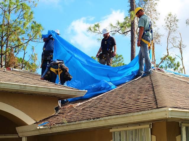 Workers spreading a blue tarp over a house roof during repairs