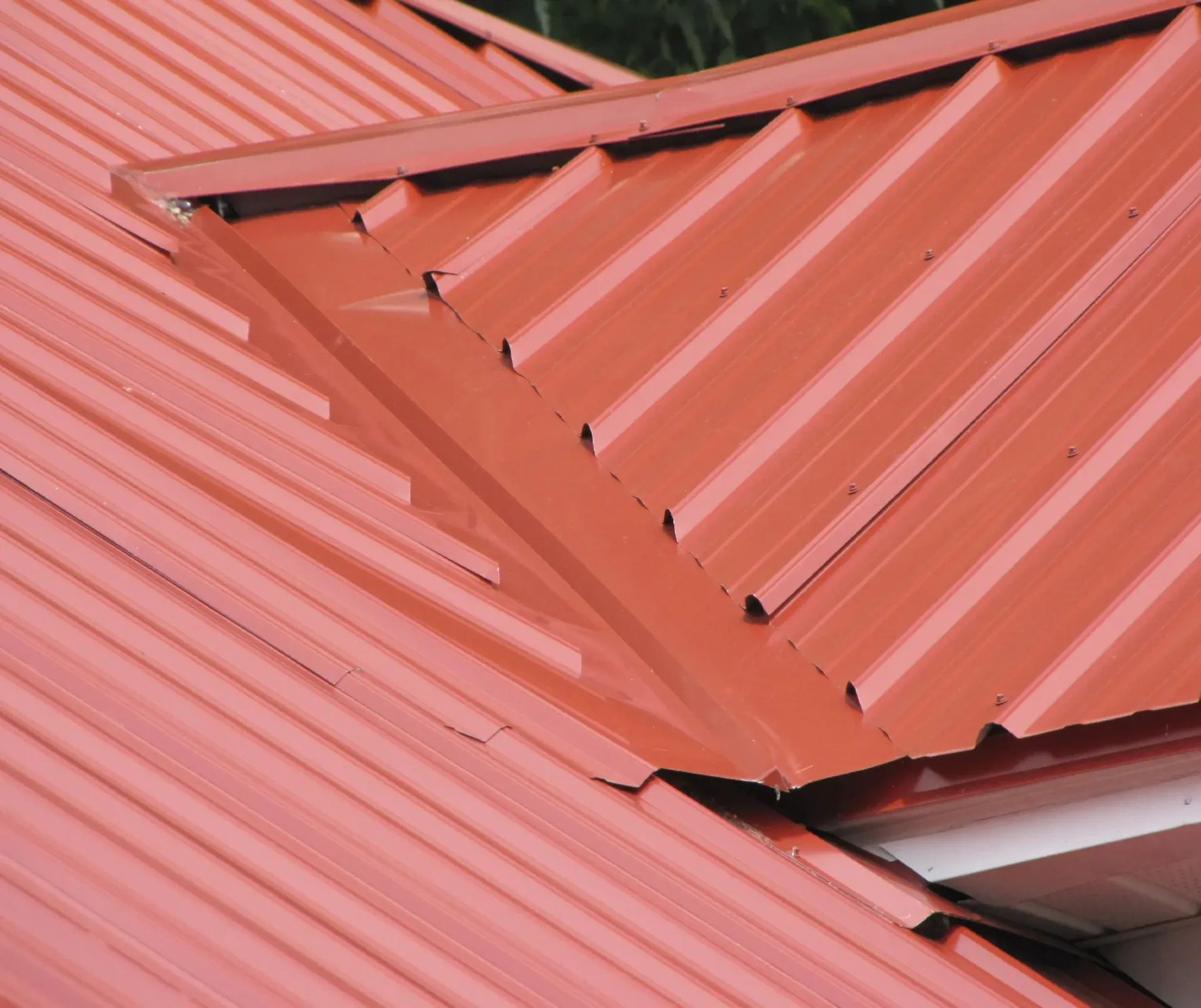 Close-up of red metal roofing panels with overlapping seams and a ridge intersection