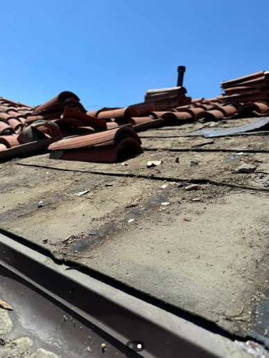 Damaged rooftop with broken concrete and red tiles under a blue sky