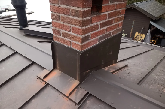 Brick chimney flashing on a gray metal roof with a vent pipe nearby