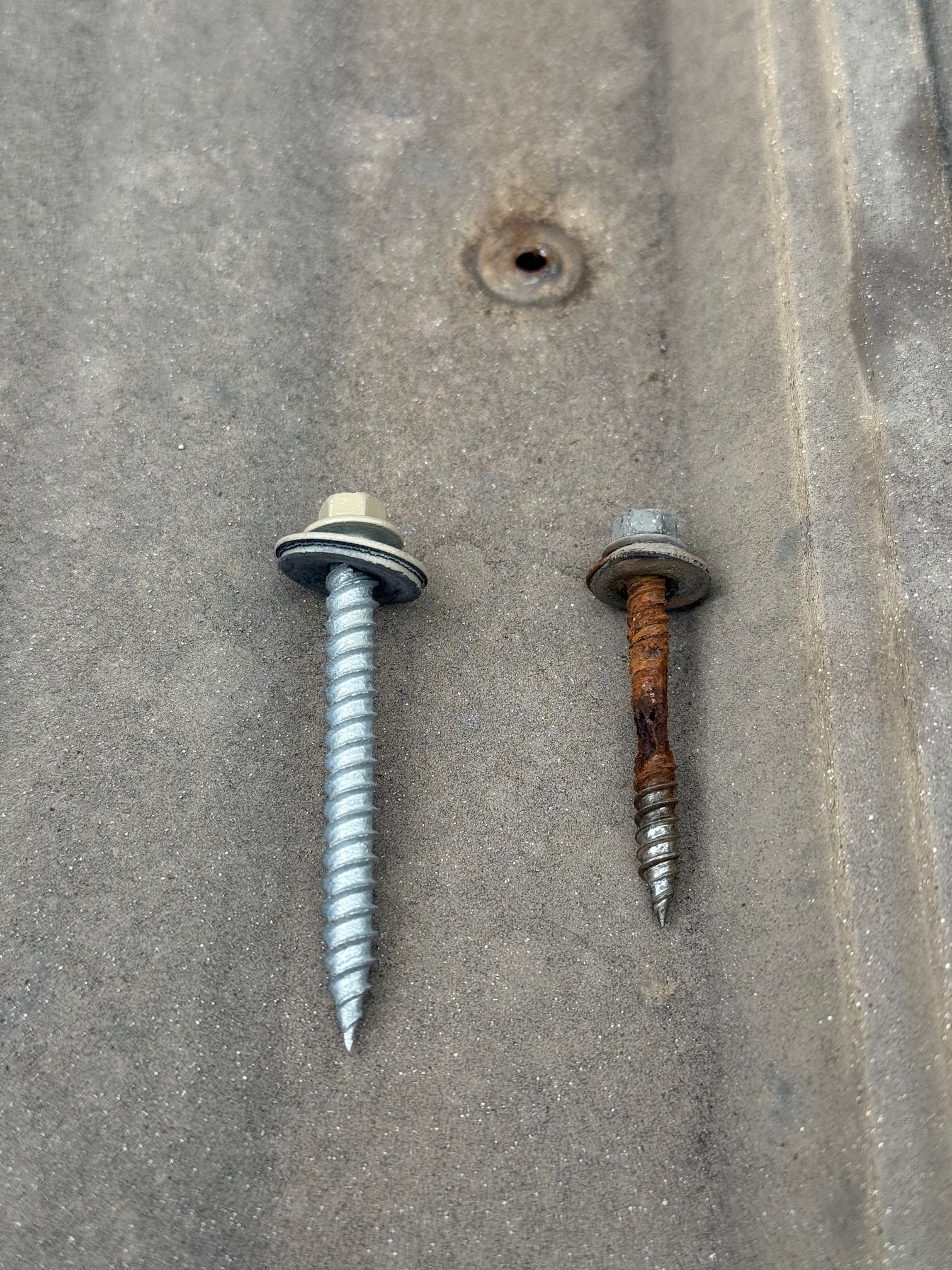 Two screws on a gray metal surface, one shiny silver and one rusty brown.