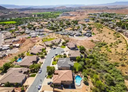 Aerial view of a suburban neighborhood with houses, roads, a pool, and desert hills in the background