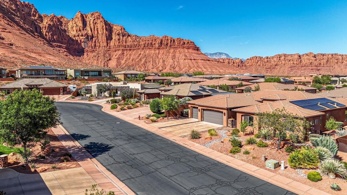 Desert resort homes with red rock cliffs and a paved road under a clear blue sky