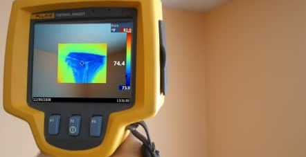 Yellow thermal camera displaying a heat map on its screen indoors