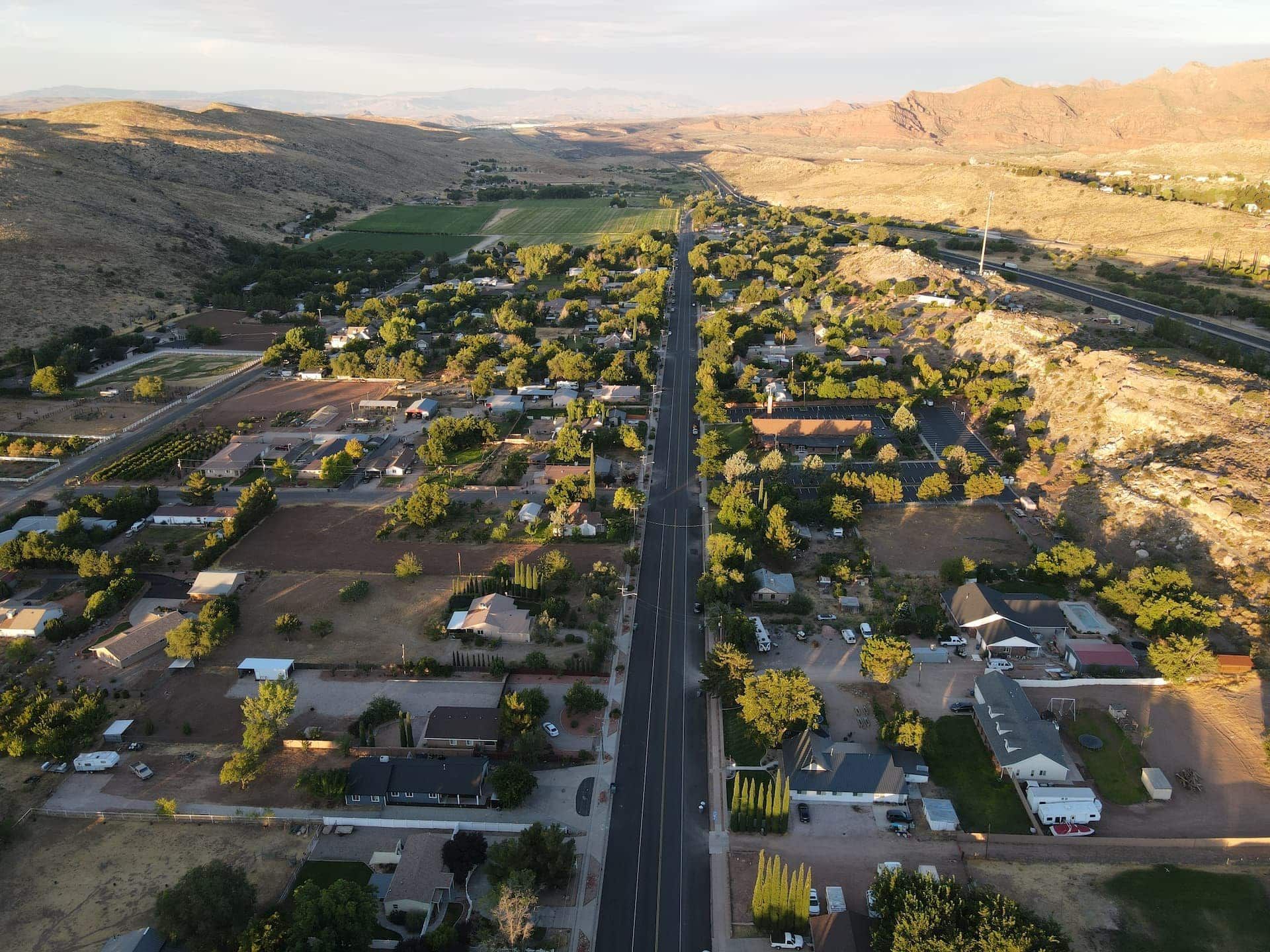 Aerial view of a suburban neighborhood with a straight road, houses, trees, and desert hills in the distance