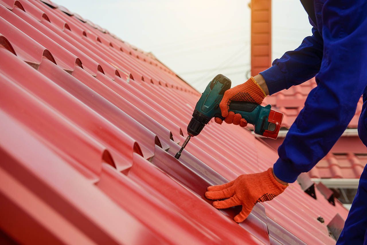 Worker using a drill to fasten red metal roofing panels on a roof