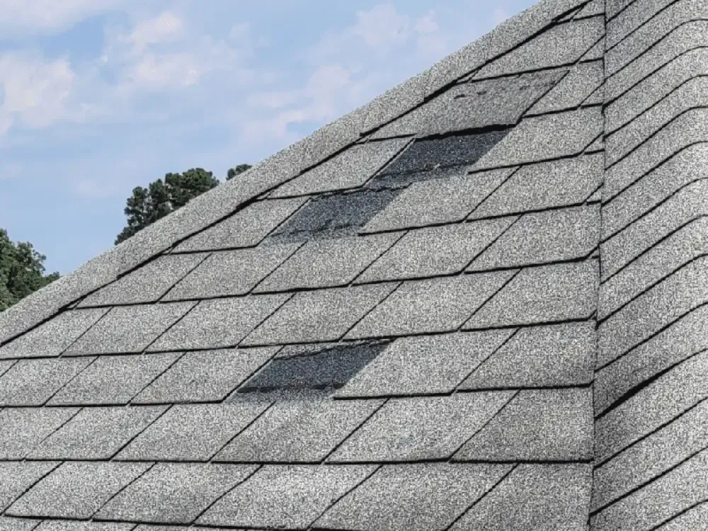 Gray shingled roof with several dark roof patches under a cloudy sky