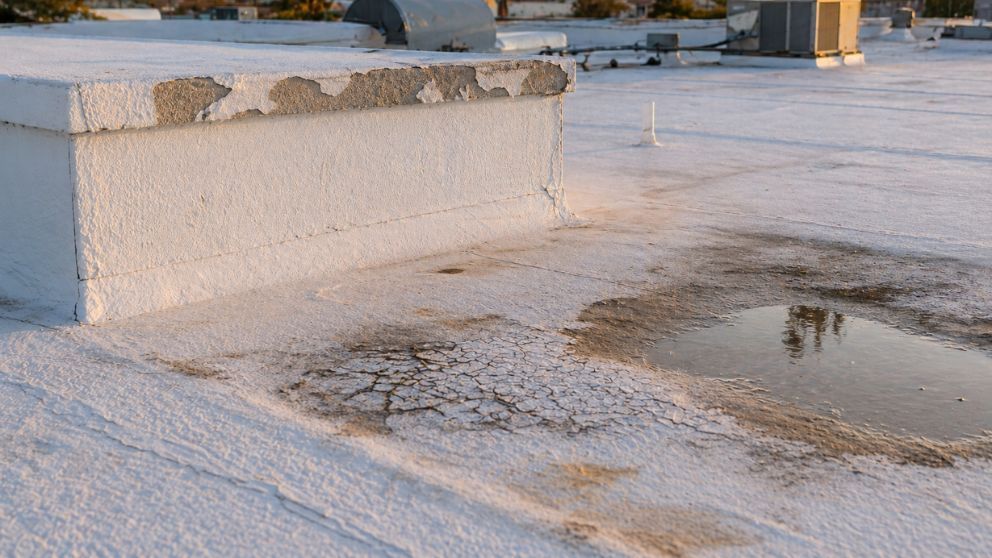 Snow-covered outdoor rooftop with a wet patch and a low white concrete wall under warm light