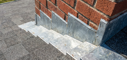 Brick wall corner with metal flashing above a stone sidewalk edge