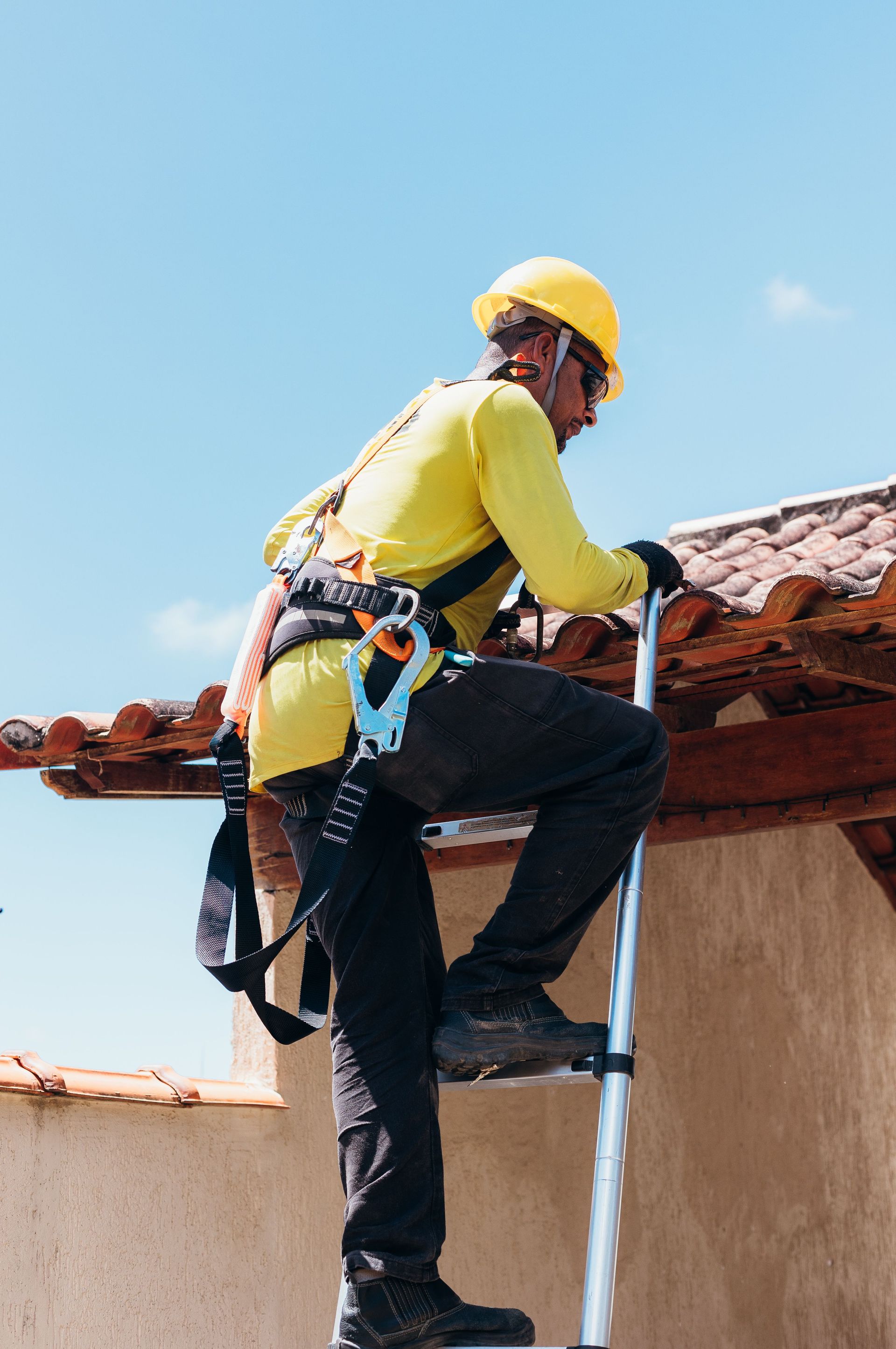 Worker in yellow safety gear climbing a roof with a harness under a blue sky