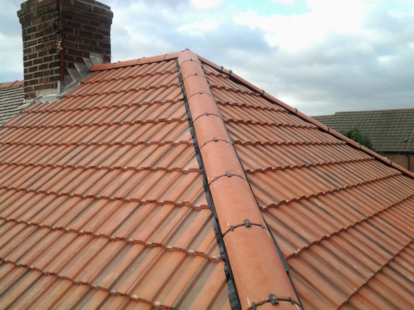 Red tiled roof with a chimney and ridge vent against a cloudy sky