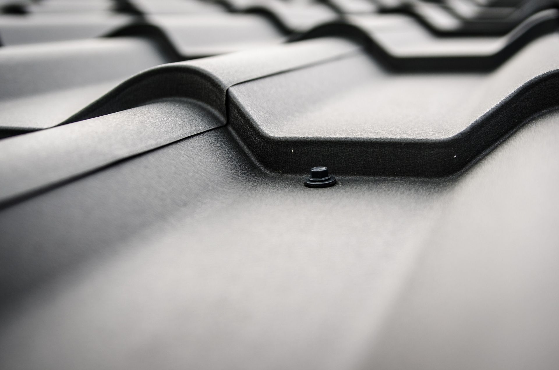 Close-up of black roof tiles with a small roof vent in soft light