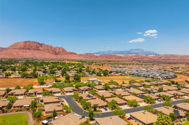 Desert suburb with tan homes, red rock cliffs, and blue sky under bright sun