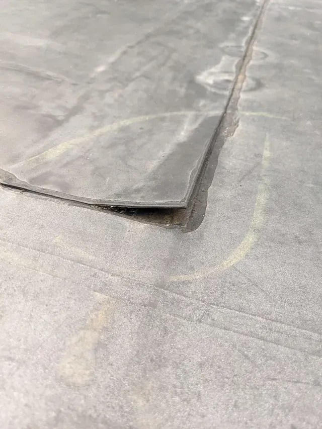 Close-up of a gray floor with a lifted seam or torn edge exposing the layer beneath