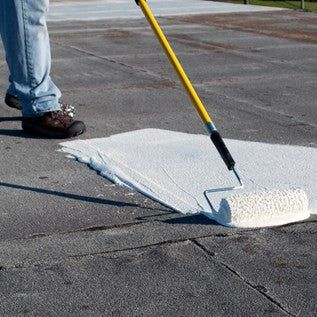 Person applying white paint to asphalt with a roller on a yellow handle