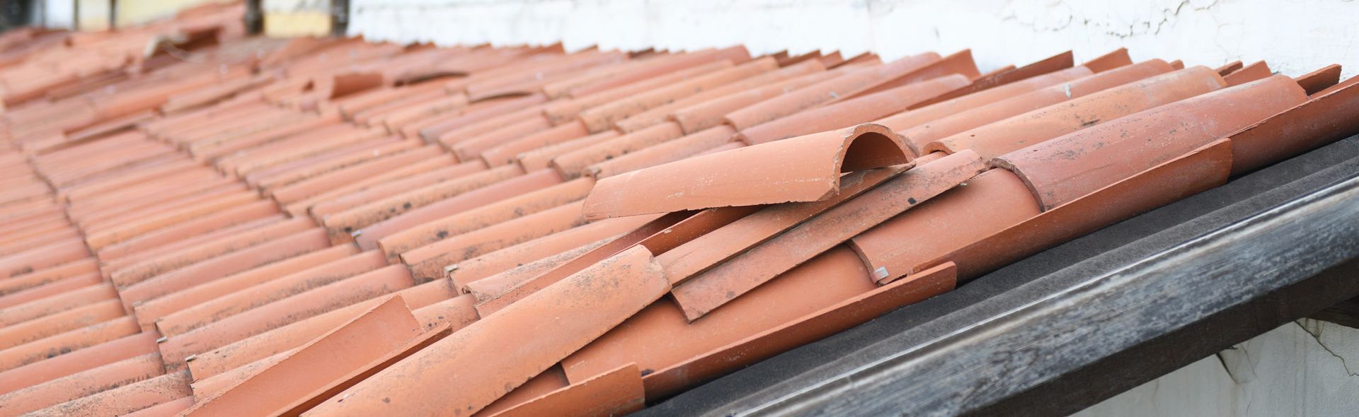 Red clay roof tiles with several loose and broken tiles near the edge.