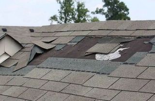 Damaged shingled roof with missing and torn sections near a roof vent