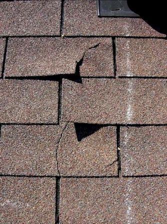 Damaged asphalt shingles on a roof with two visible holes and a crack.