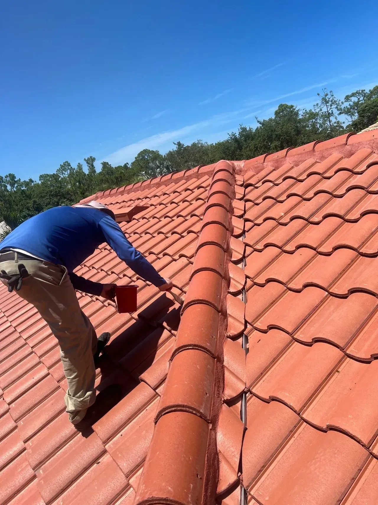 Worker on a red-tiled roof repairing tiles under a clear blue sky