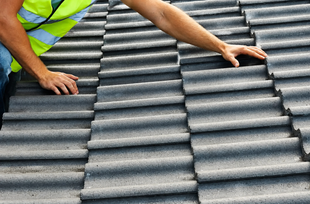 Hands inspecting a gray corrugated roof with a leaf and green safety vest visible
