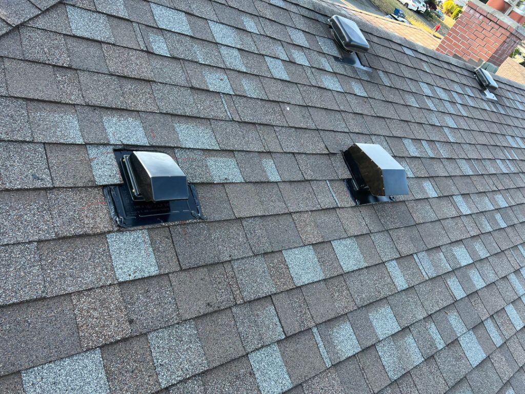 Roof shingles with two small black vents on a sloped rooftop