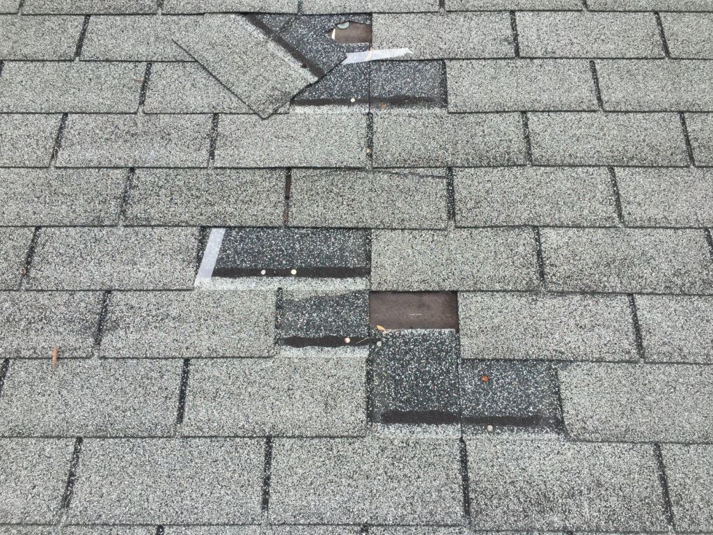 Damaged gray shingle roof with missing and patched sections