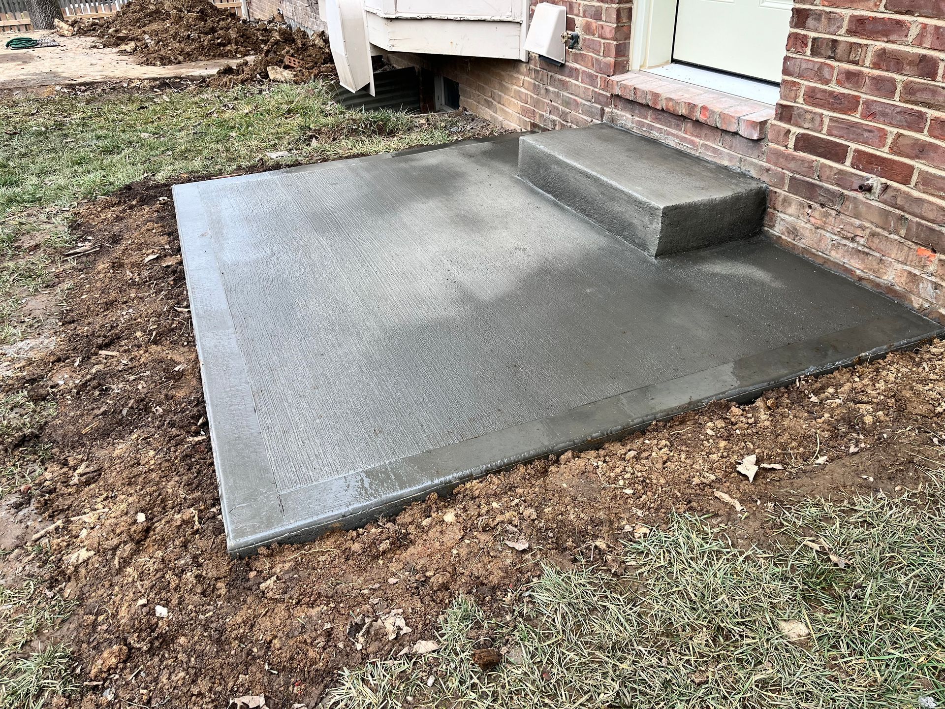 A concrete walkway is being built in front of a brick house.