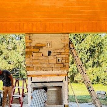 A man is standing next to a ladder in front of a brick fireplace.