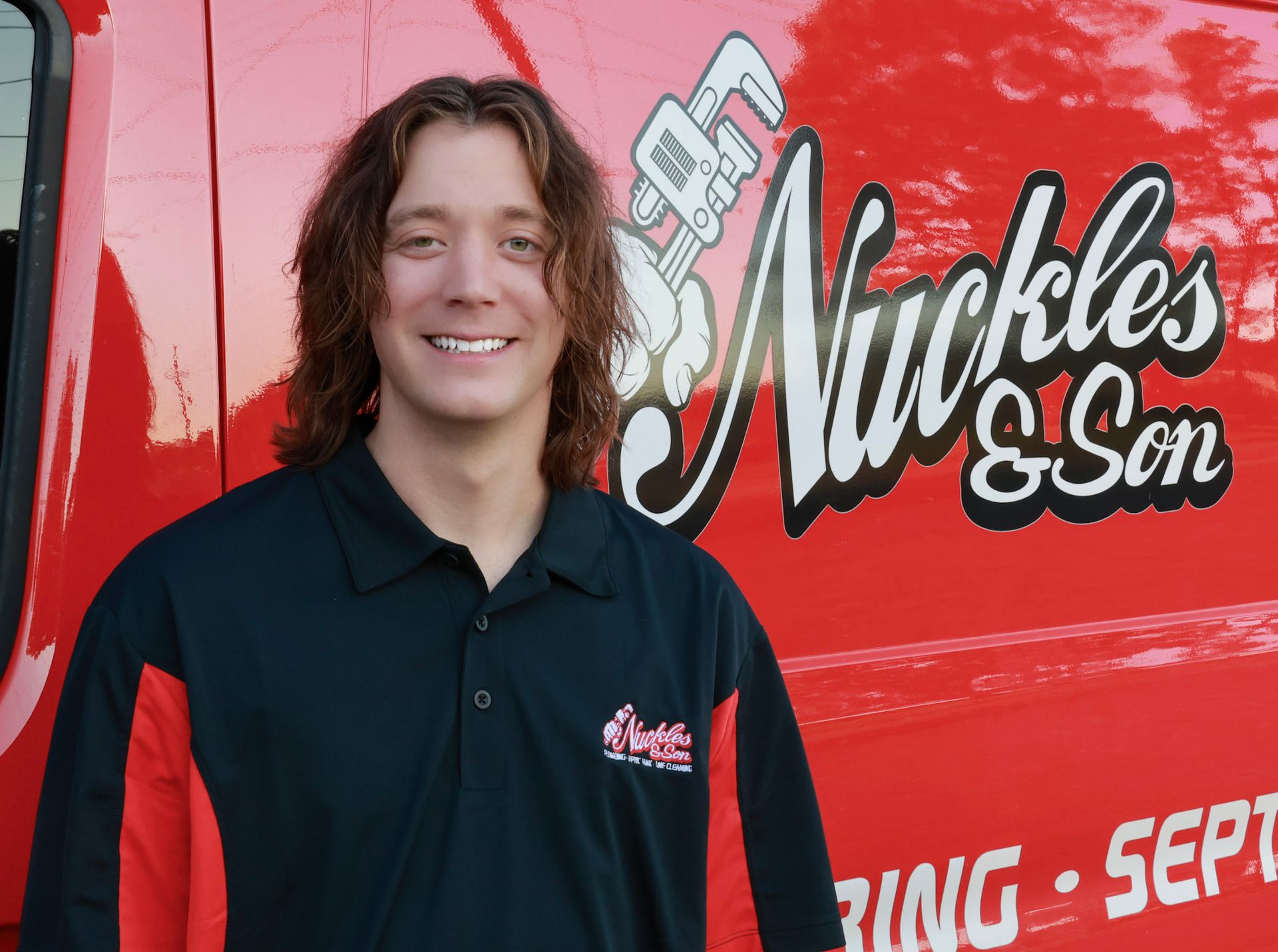 Smiling person in black shirt standing beside a red Nuckles & Co. truck