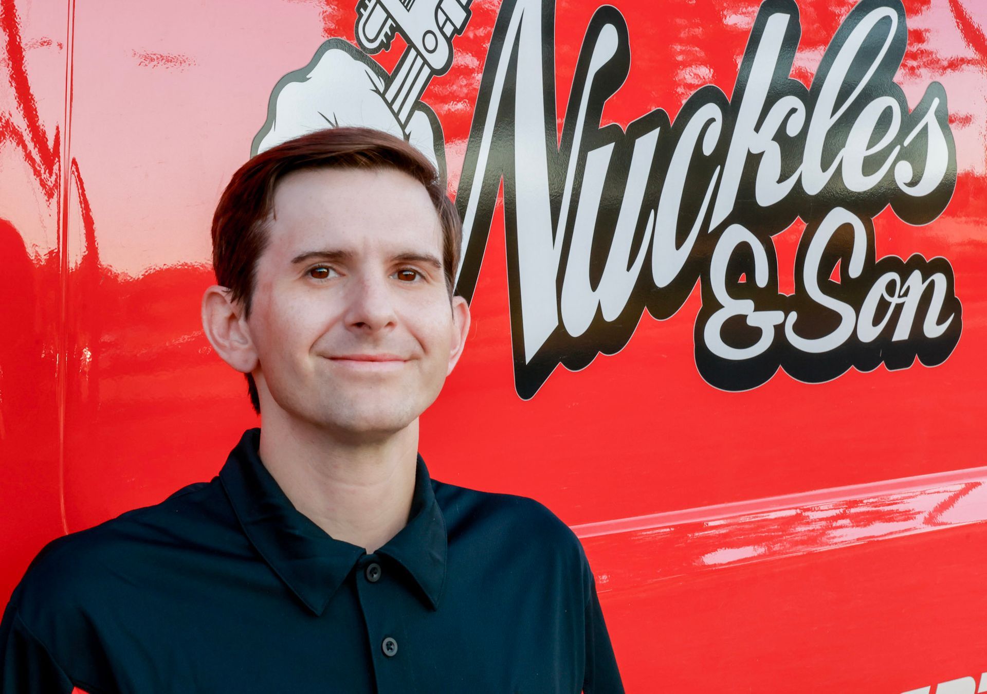 Man standing in front of a bright red Nickles & Son truck logo, wearing a dark shirt and slight smile
