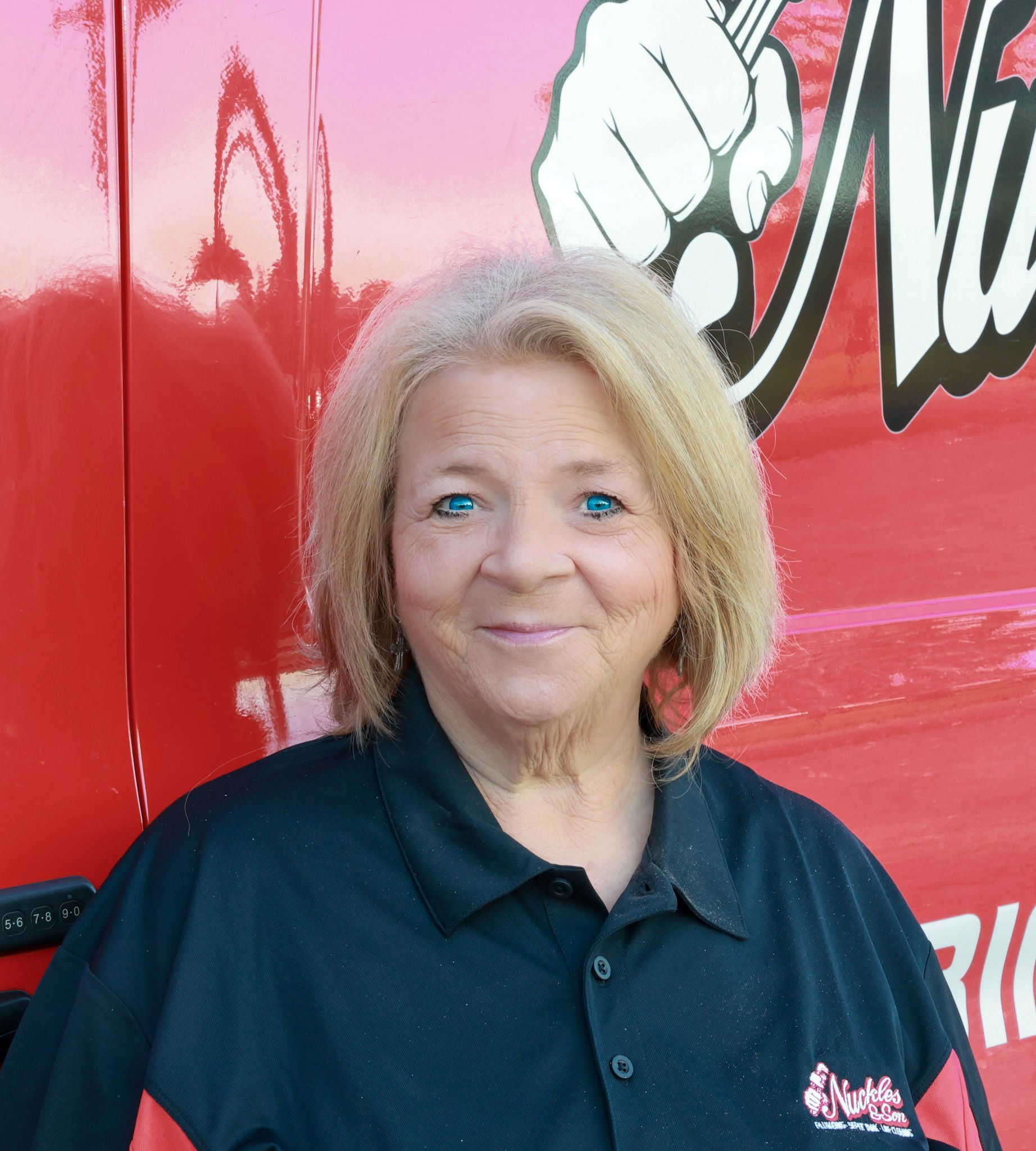 Smiling person in a dark shirt standing before a red vehicle backdrop