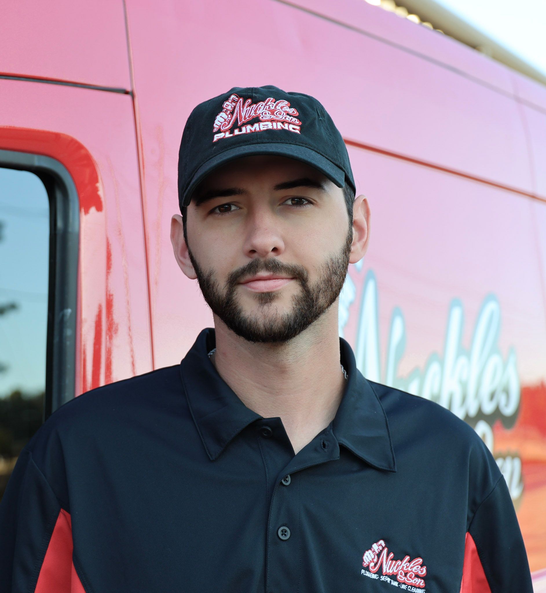 Man in black cap and shirt standing beside a pink food truck