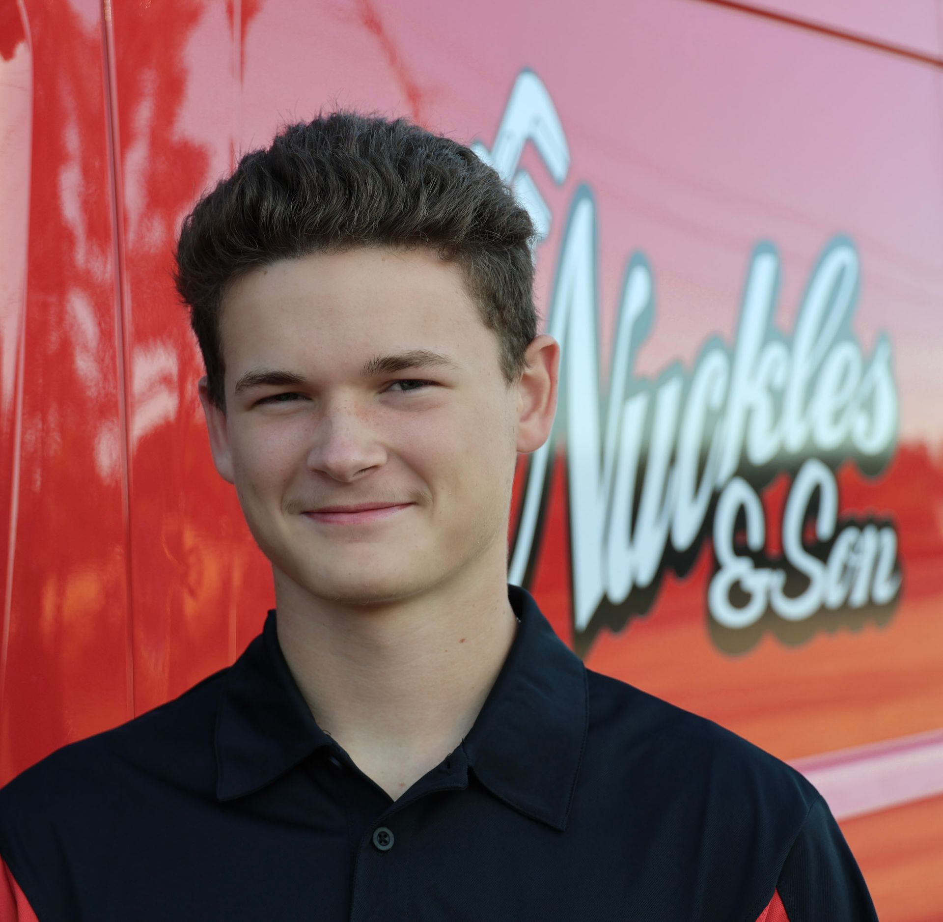 Smiling person in a black shirt standing before a red Muckles & Son truck